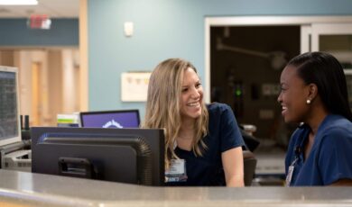 Two female nurses sitting at nurse station engaged in conversation