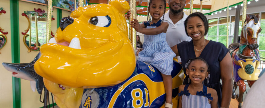 Family smiles beside NC A&T Bulldog carousel figure.