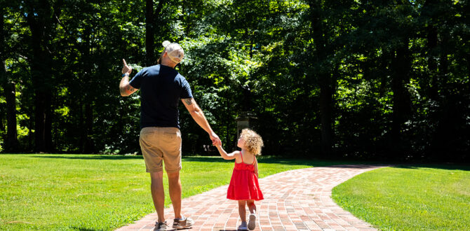 Father and daughter walking on sunlit path.