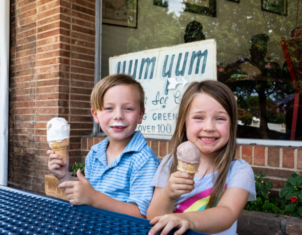 Two smiling children enjoy ice cream outside a local shop in Greensboro, NC, one of the many family-friendly places in the Carolina Core.