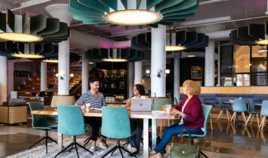 A male and two female professionals sit around a desk in a modern office common area