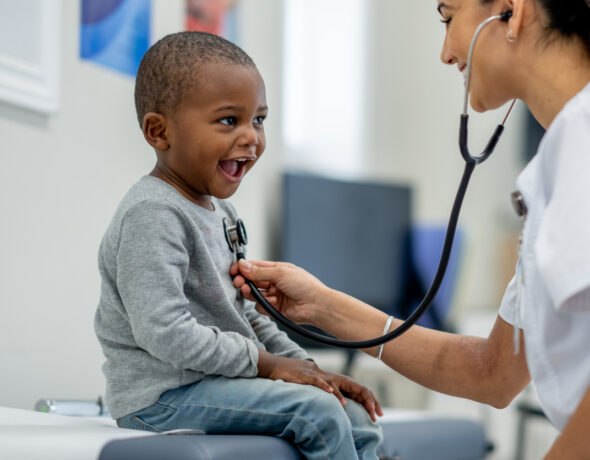 A doctor listens to the heartbeat of a smiling, small child during a checkup.