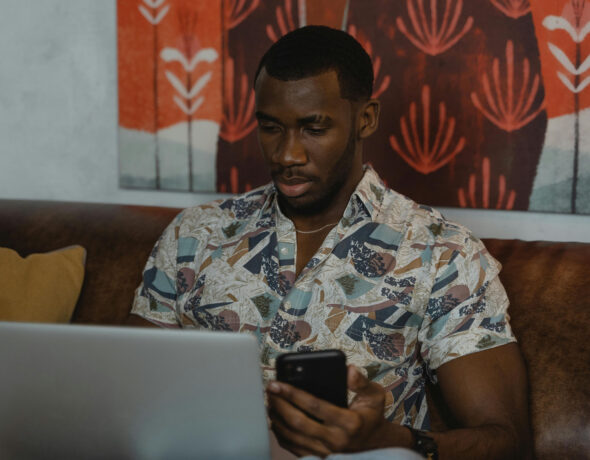 Black man in White and Blue Floral Button Up Shirt Holding Black Smartphone