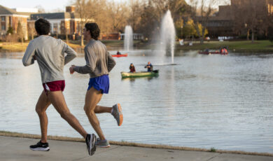 Two people take an evening run around Lake Mary Nell where people are canoeing in the background.