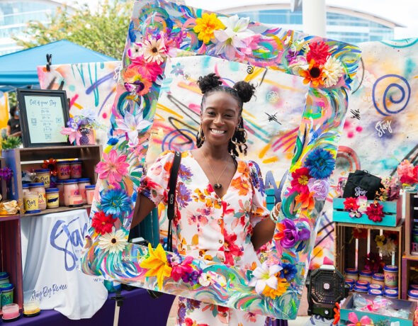 Woman holding a large floral wooden frame at the Black Luxe Expo.