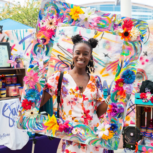 Woman holding a large floral wooden frame at the Black Luxe Expo.